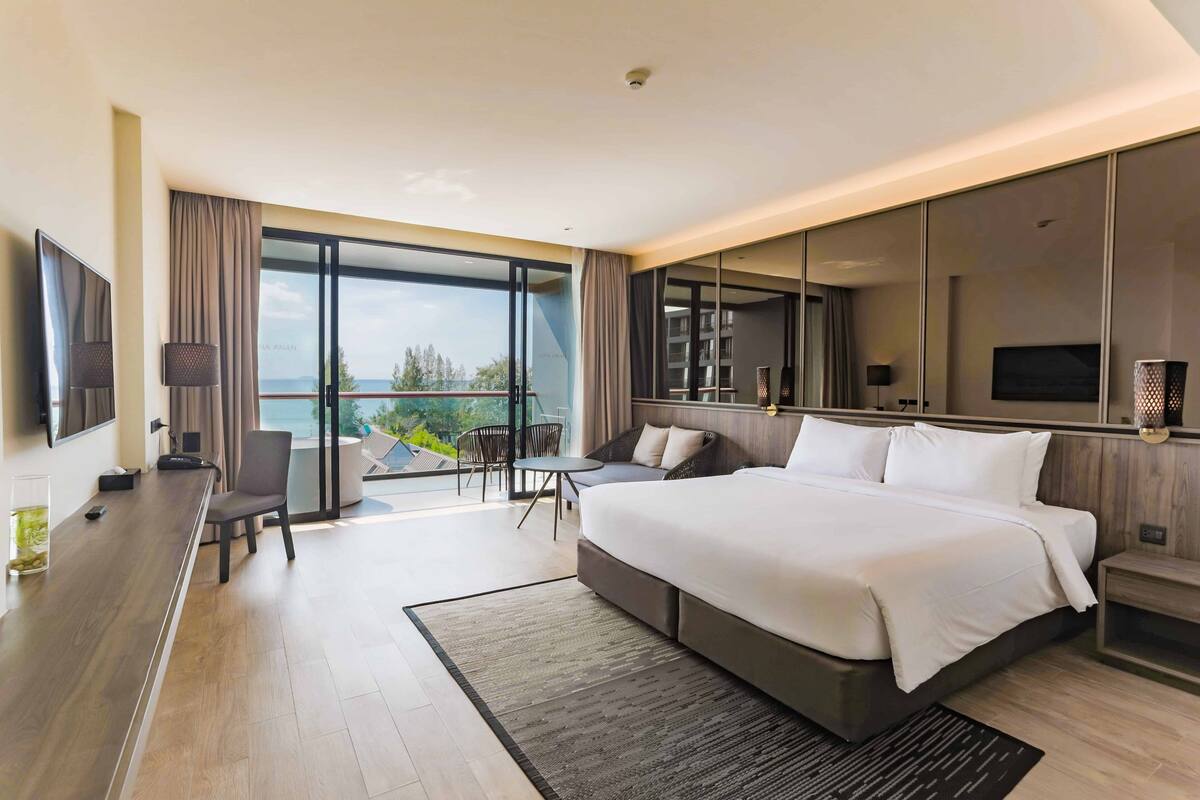 Une chambre d’hôtel moderne avec un grand lit, un bureau et un balcon offrant une vue agréable.