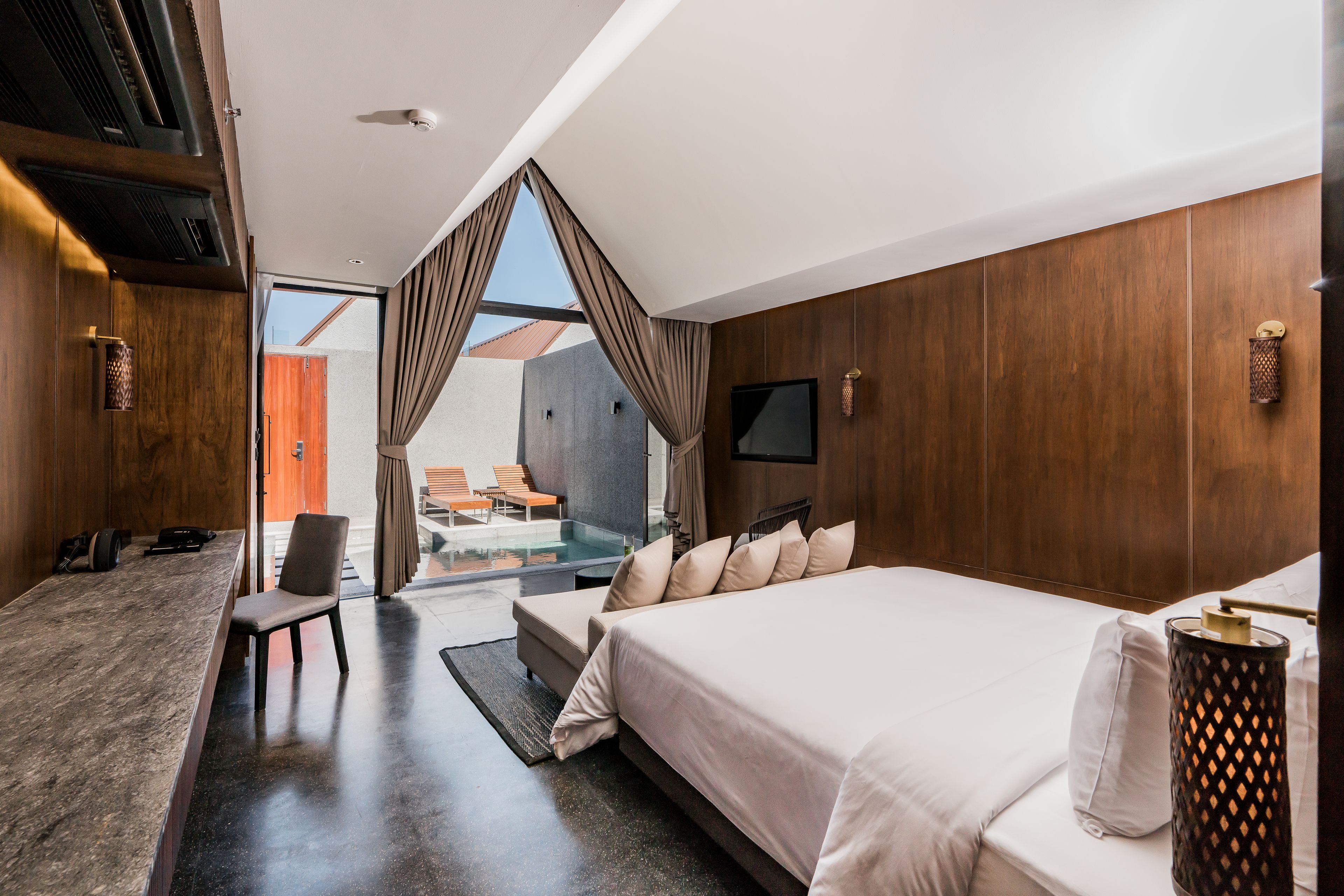 A modern hotel room with a large bed, a desk, and a view of the outdoor area.