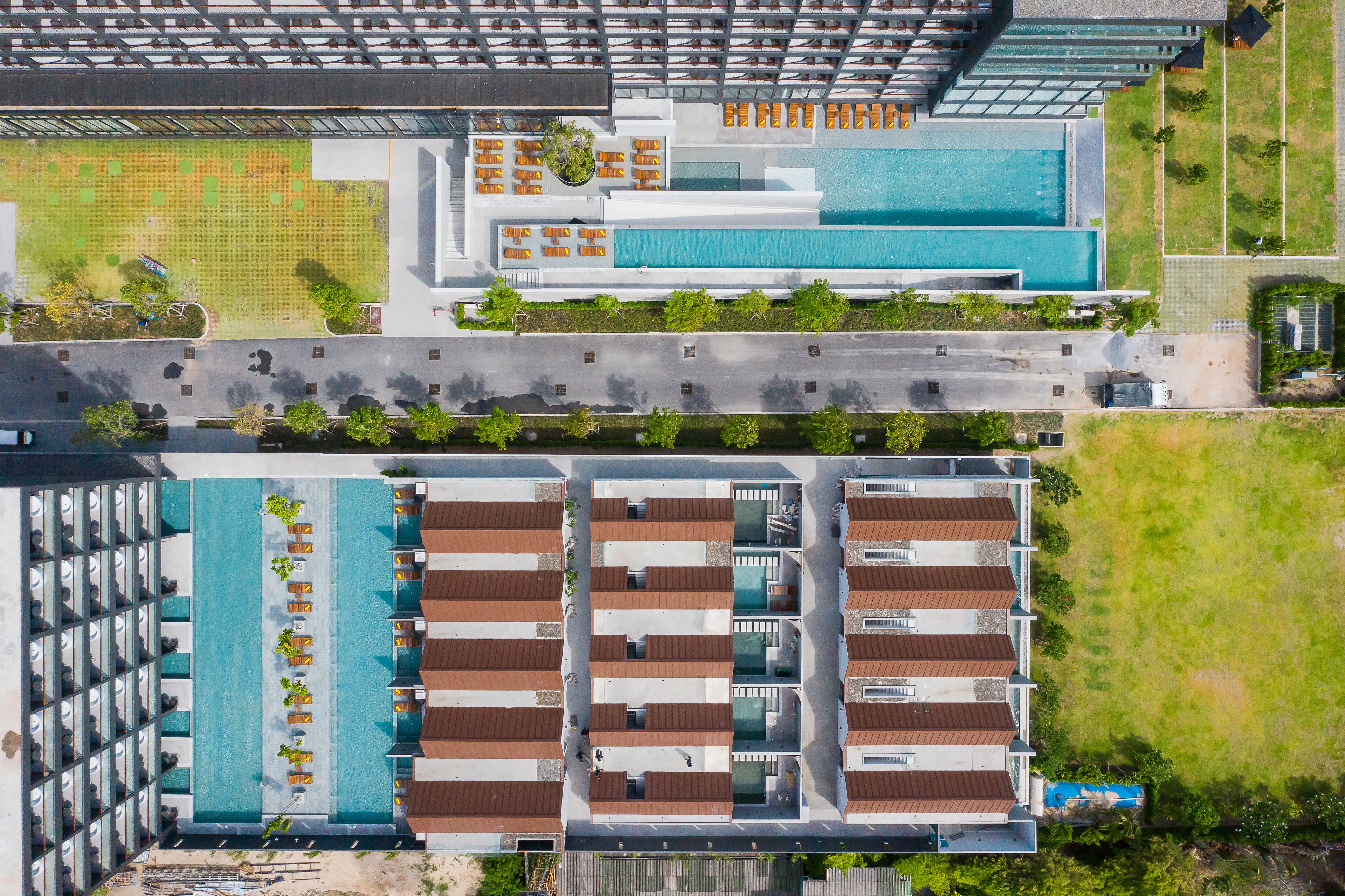 An aerial view of a hotel with multiple swimming pools, a parking area, and a road.