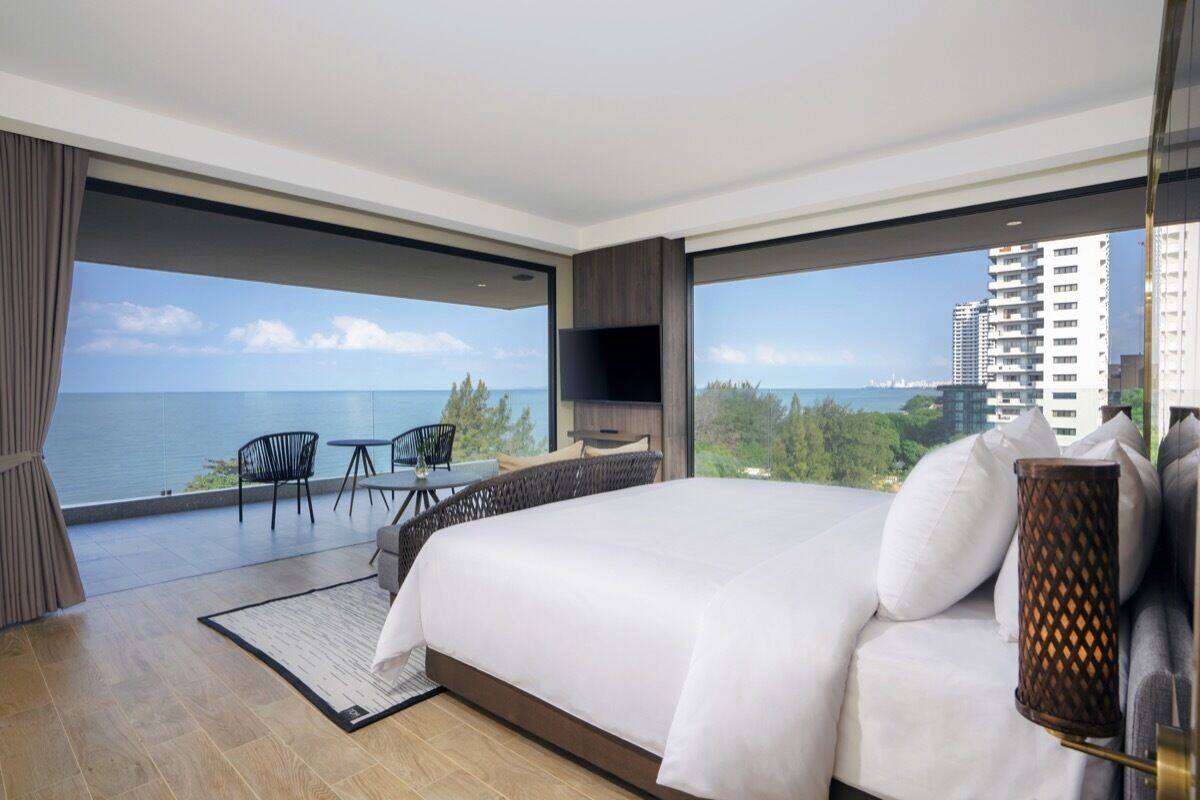 Une chambre moderne avec un grand lit, une télévision et un balcon offrant une vue sur l’océan et les bâtiments.