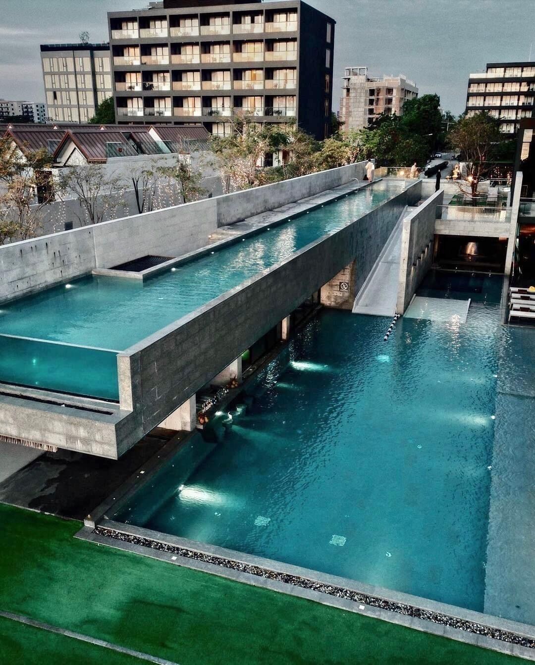 A rooftop swimming pool with a concrete bridge, surrounded by buildings.