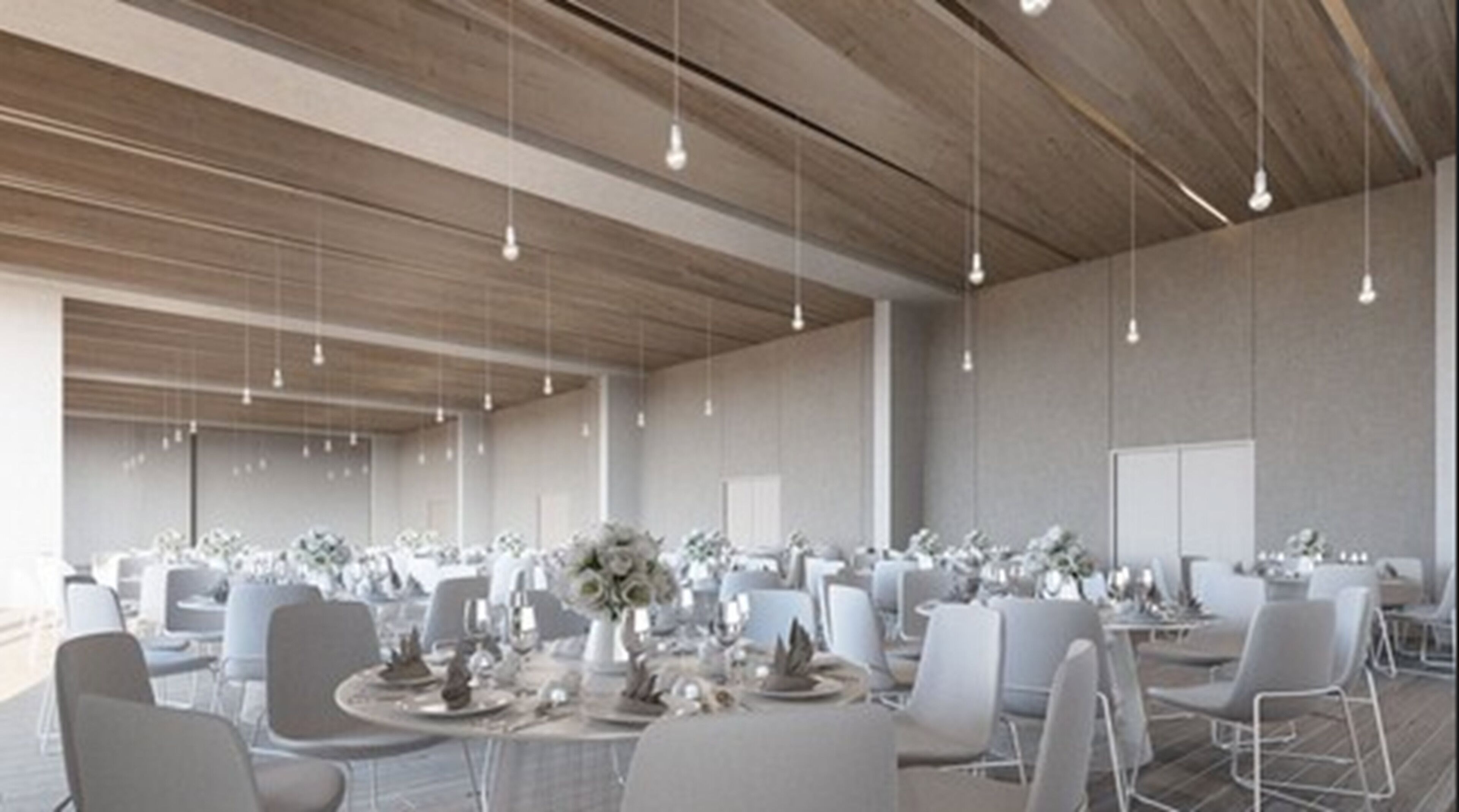 A spacious indoor venue with multiple tables set for dining, featuring white tablecloths and floral centerpieces.