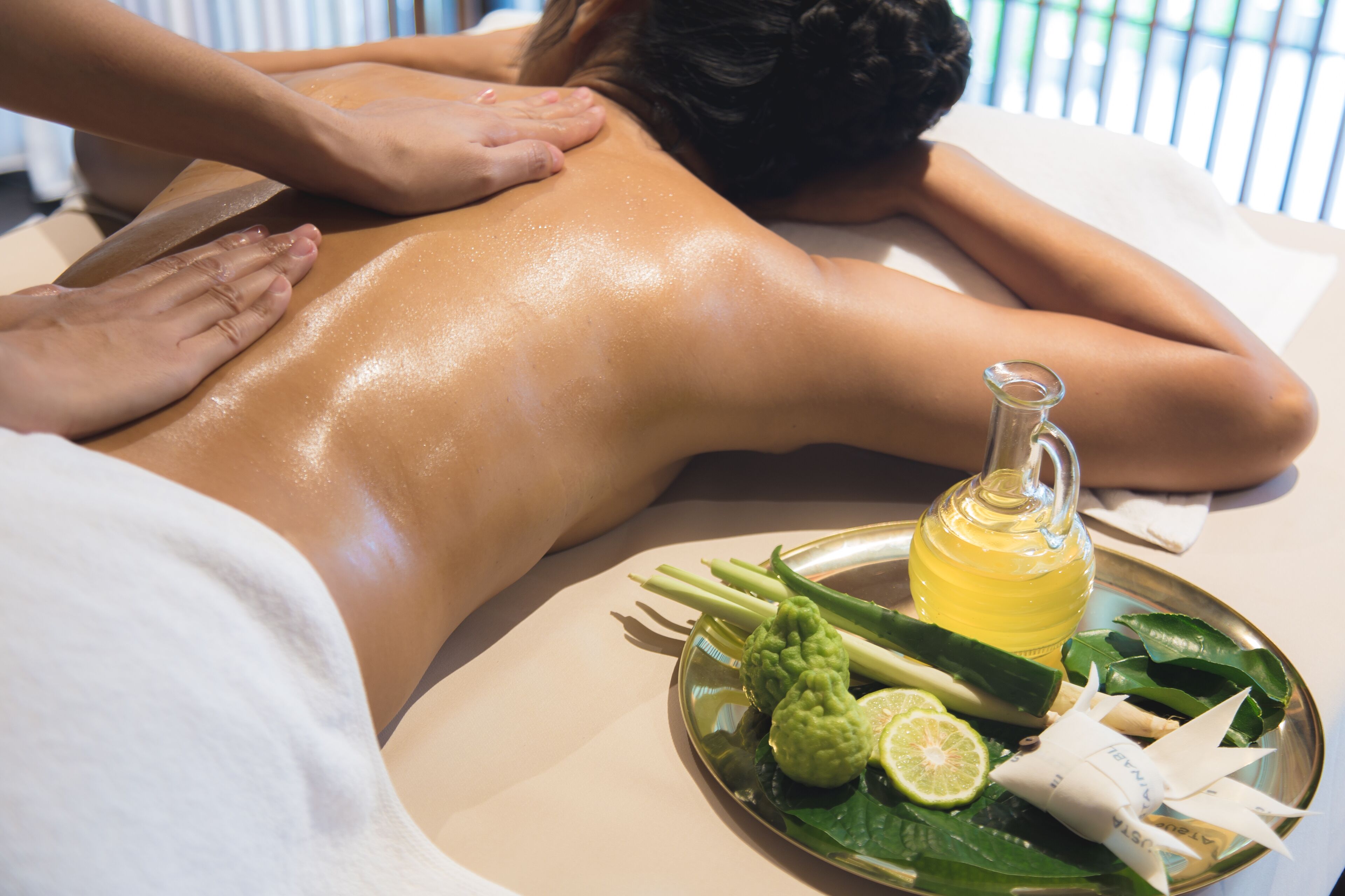 A massage therapy session with a tray of herbal compresses and a bottle of oil.