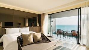 Une chambre d’hôtel avec un lit, un canapé, une télévision et un balcon donnant sur la mer.