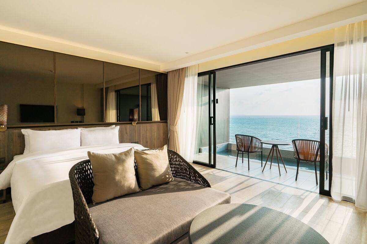 Une chambre d’hôtel avec un lit, un canapé, une télévision et un balcon donnant sur la mer.