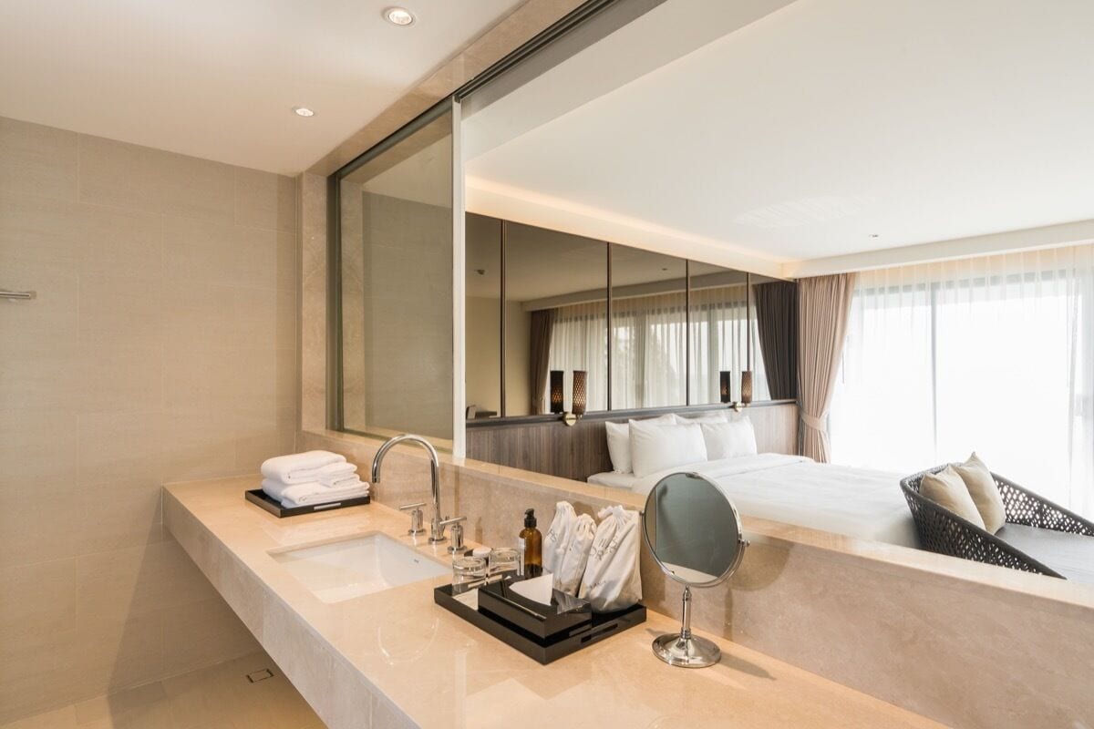 Un baño de hotel moderno con un espejo grande, un lavamanos y una mesita de noche con una bandeja de toallas.