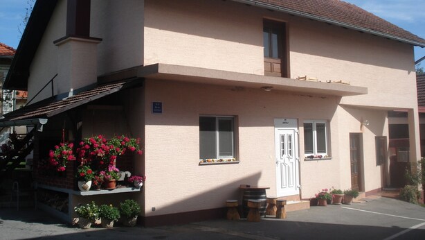 Un bâtiment à deux étages, doté d’un toit plat, d’un balcon et d’un petit espace porche agrémenté de plantes en pot.