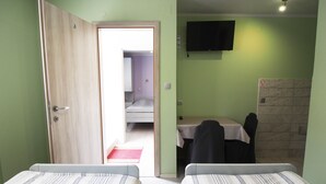 Une chambre avec deux lits, une télévision, un bureau avec une chaise et une porte menant à la salle de bain.