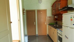 Une cuisine de taille réduite, dotée de deux portes en bois, d’un réfrigérateur, d’une cuisinière et d’un évier.