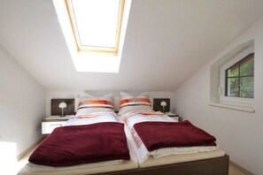 A bedroom with a skylight, a bed with two pillows, a bedside table with a lamp, and a window.