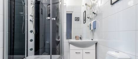 Un baño moderno con ducha envuelta en vidrio, inodoro blanco, lavamanos y un cuadro en la pared.