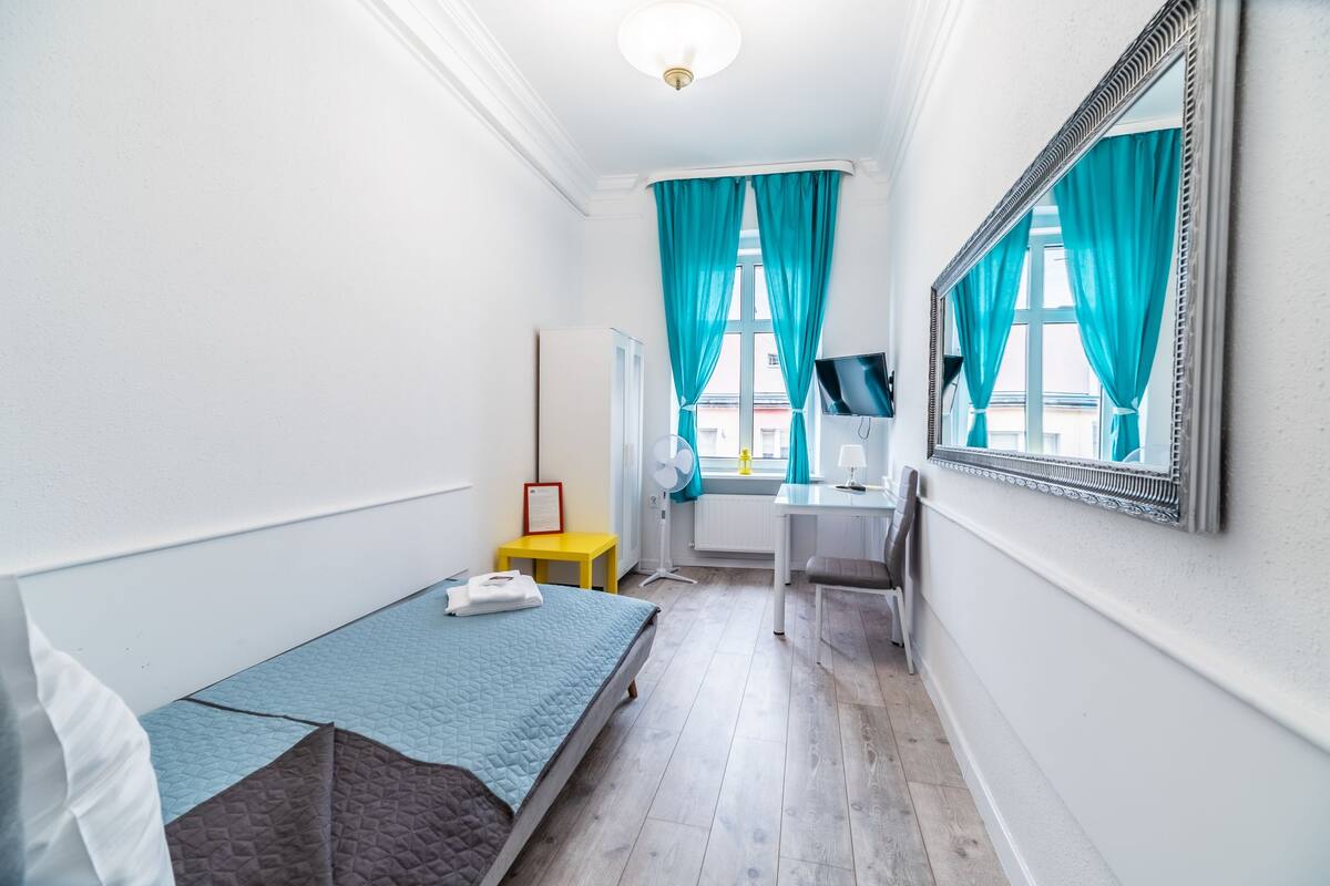 A small, well-lit room with a bed, a desk, and a mirror.