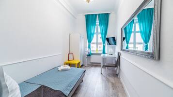 A small, well-lit room with a bed, a desk, and a mirror.