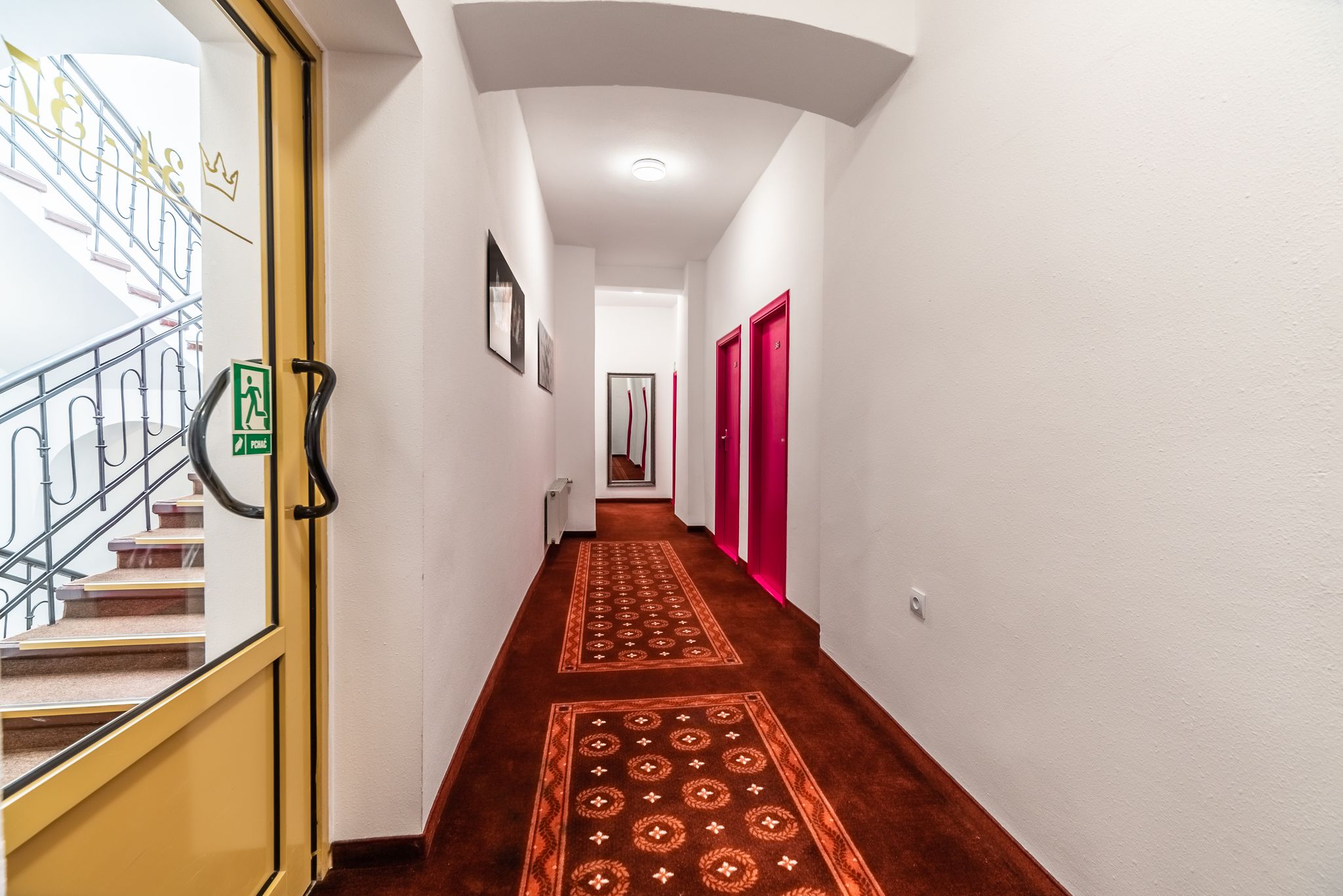 A hallway with a carpeted floor, a staircase, and a door with a sign.