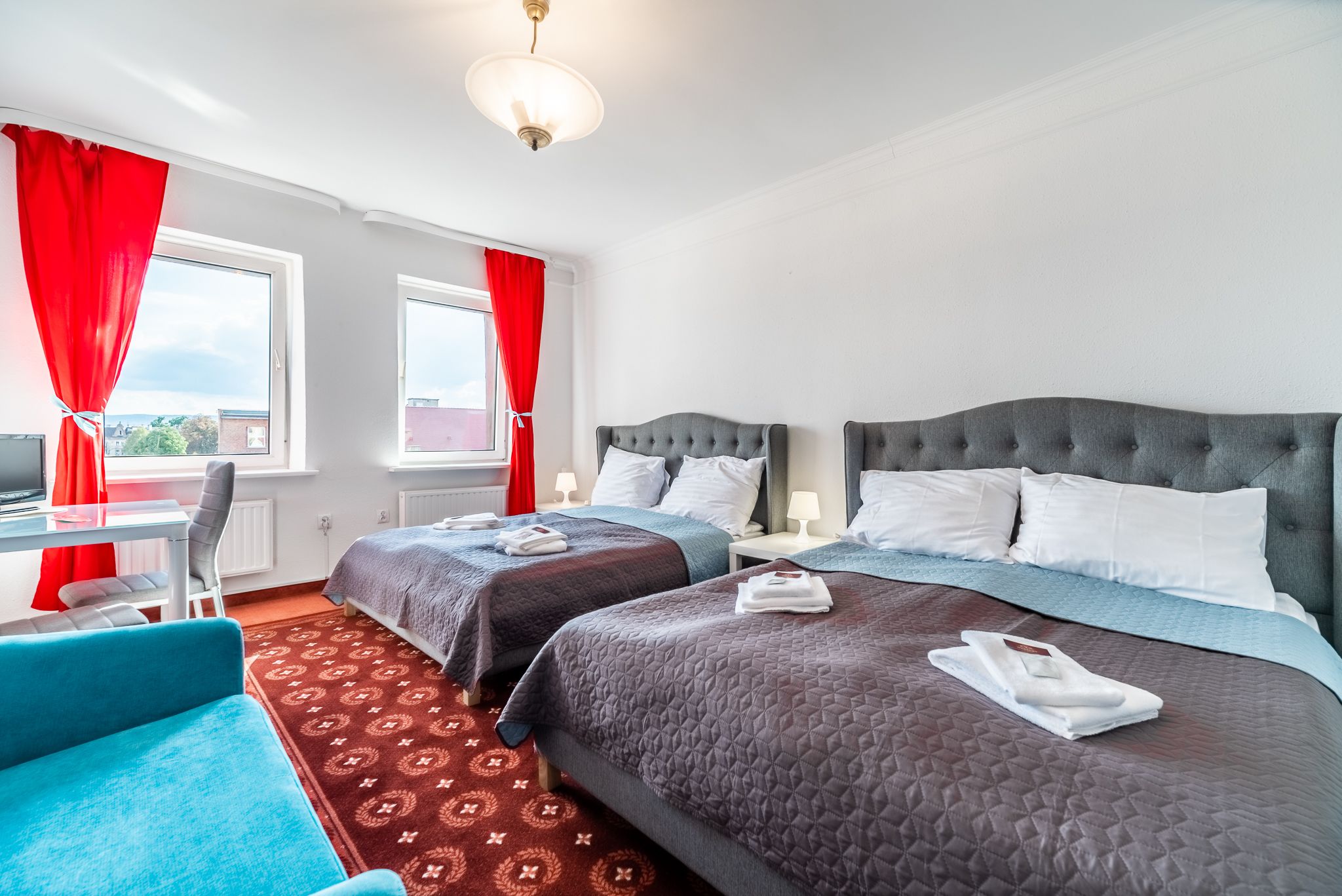 Hotellihuone, jossa on kaksi sänkyä, työpöytä ja tuoli.