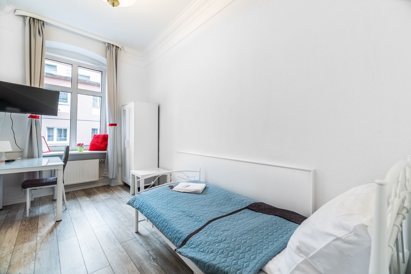 Habitación de hotel con cama, escritorio, silla, televisor y ventana con cortinas.