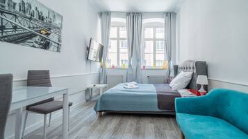 Ein modernes Hotelzimmer mit Bett, Schreibtisch, Sessel, Sofa und einem großen Fenster mit Vorhängen.