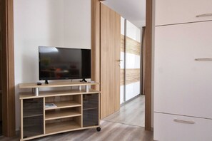 Une chambre moderne avec un téléviseur posé sur un meuble en bois, une armoire et une porte donnant sur une autre pièce.