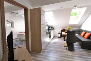 A modern kitchen with a dining area, a sofa, and a television.