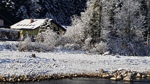 A house surrounded by snow-covered trees and a river. - Apartment Sonnenblick - Apartments Winkler (Bad Goisern am Hallstättersee)