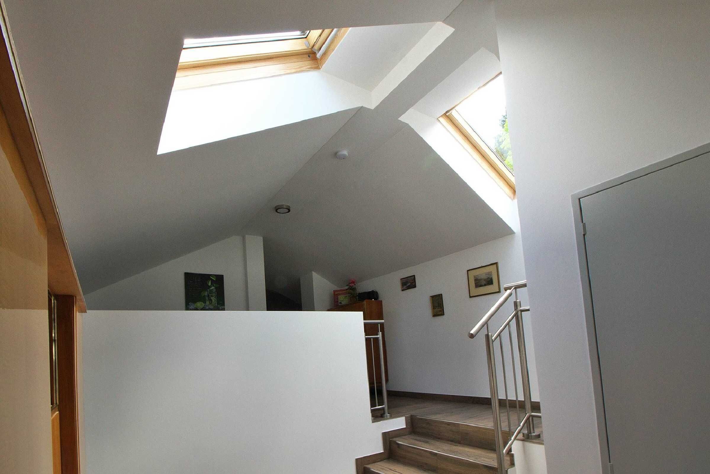 Un escalier avec un puits de lumière, des murs blancs et une rampe en métal.