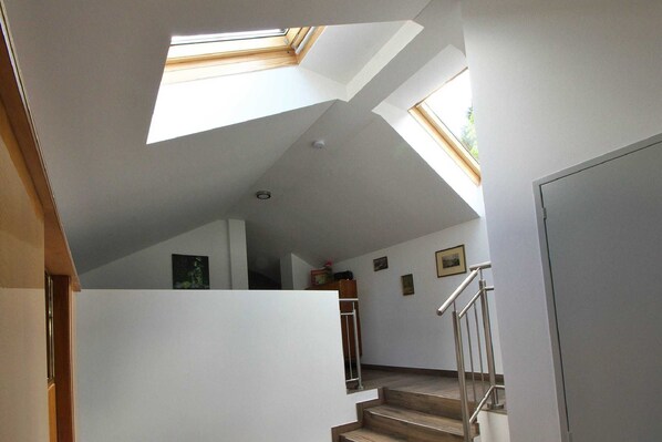 Un escalier avec un puits de lumière, des murs blancs et une rampe en métal.