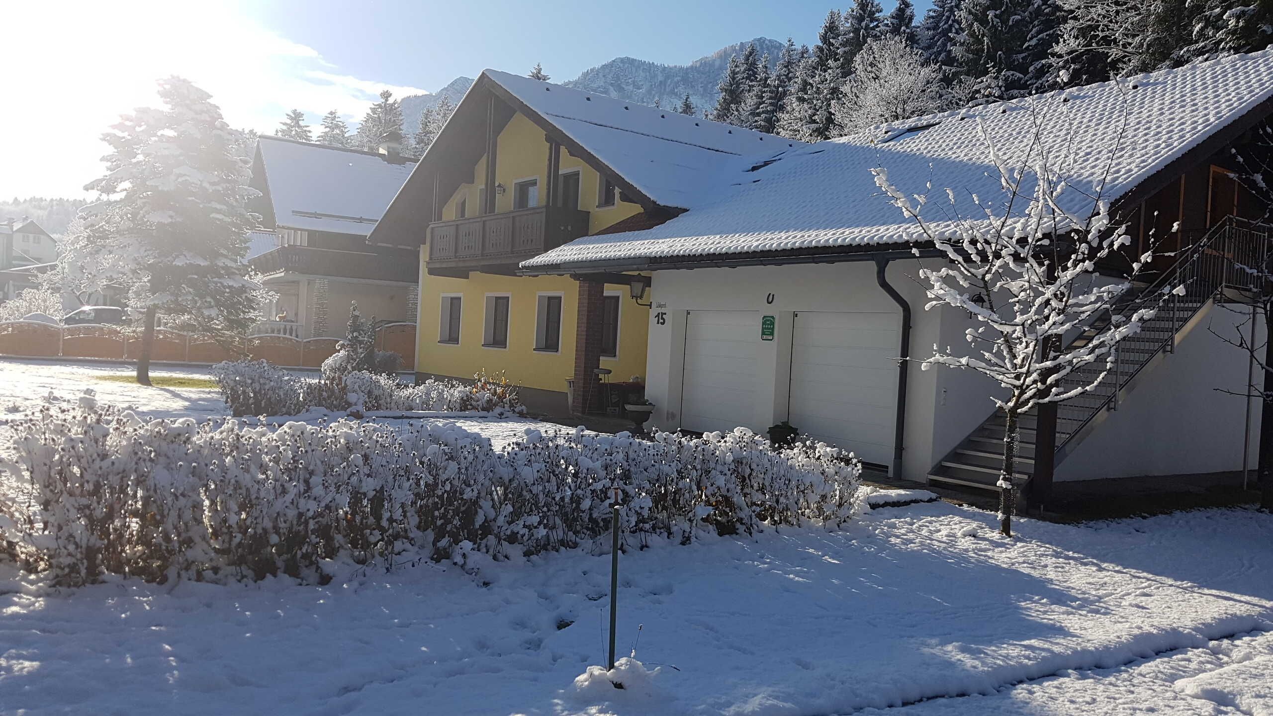 A snow-covered building with a yellow facade, a garage, and a staircase leading to the entrance.