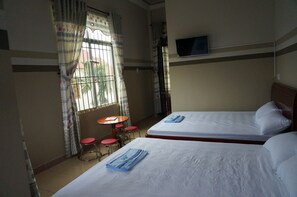 Une chambre d’hôtel avec deux lits, un téléviseur fixé au mur, une petite table avec des tabourets et une fenêtre avec des rideaux.