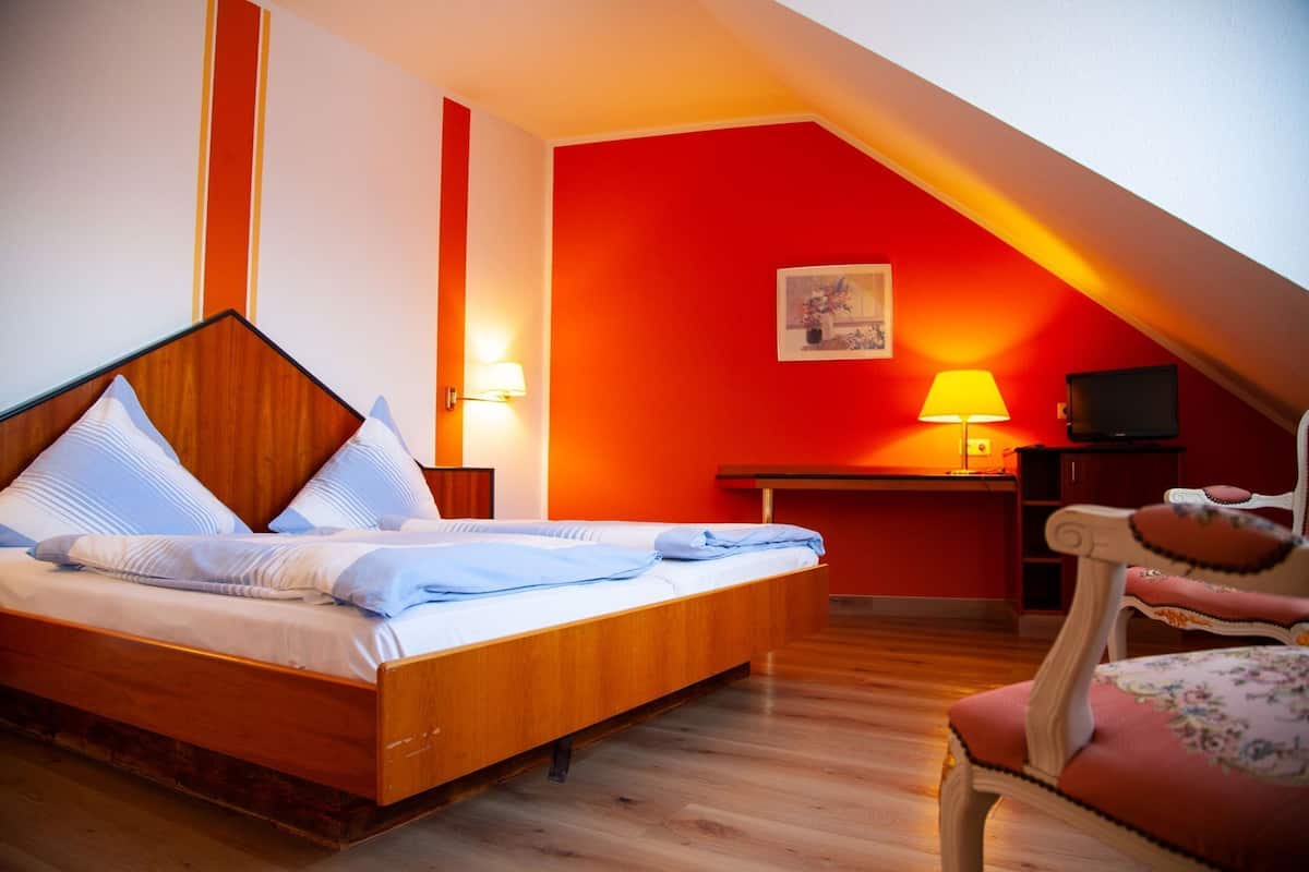 Ein Schlafzimmer mit einem Holzbett, einem Schreibtisch mit Lampe, einem Sessel und einem Fernseher.