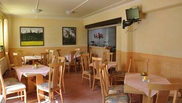 Uma sala de jantar com mesas e cadeiras de madeira, uma televisão presa na parede e obras de arte nas paredes.