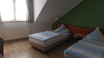 A room with two beds, a radiator, a window with curtains, and a telephone on the wall.