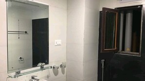 Une salle de bain avec un lavabo blanc, une étagère en verre au-dessus, un miroir, des toilettes et un espace douche.