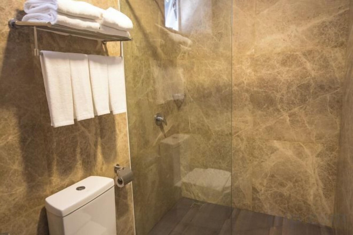 Ein Badezimmer mit Marmorwand, Toilette, Duschbereich und einem Handtuchhalter mit Handtüchern.