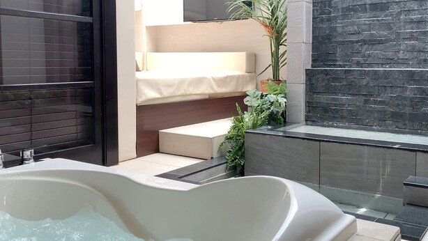 A modern bathroom with a freestanding bathtub, a shower area, and a small seating area with a bench and potted plants. - Hotel Asia - Adults Only (Gifu)