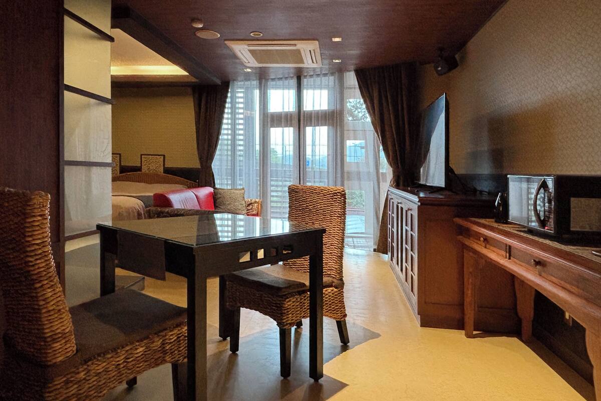 A hotel room with a dining area, a sofa, a television, and a window with curtains.