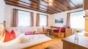 A cozy room with a wooden bed, a desk, and a chair. There are curtains on the windows, and a painting on the wall. - Apartment Talblick - Biohof Maurachgut (Bad Hofgastein)