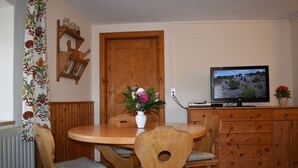 Ein Essbereich mit Holztisch, Stühlen, einem Blumenstrauß, einem Fernseher auf einem Schrank und einem Holzschrank.