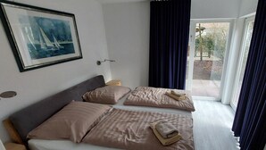 Ein Zimmer mit einem Bett, einem Bild, einem Fenster mit Vorhängen und Blick ins Freie.