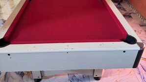 Un tavolo da biliardo con superficie in feltro rosso, circondato da un pavimento a motivi marmorei.