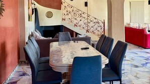 Zona pranzo con pavimento in marmo, tavolo centrale circondato da sedie e una scala con ringhiera decorata con motivi floreali.