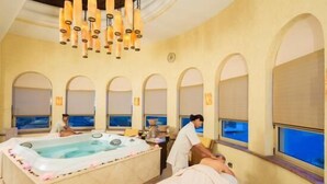 Ein Wellnessraum mit einer großen Badewanne, Rundbogenfenstern und einer Deckenleuchter.