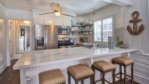 Een moderne keuken met een groot kookeiland, roestvrijstalen apparatuur en een plafondventilator.