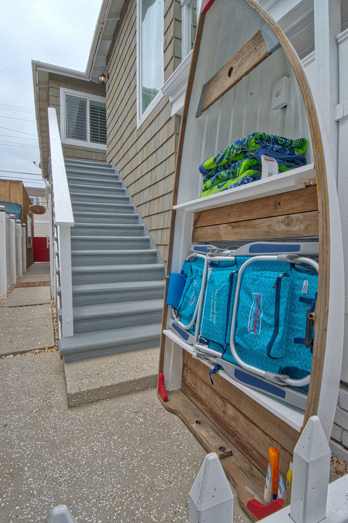 A wooden staircase leading to a beach house with a built-in storage unit containing beach gear.