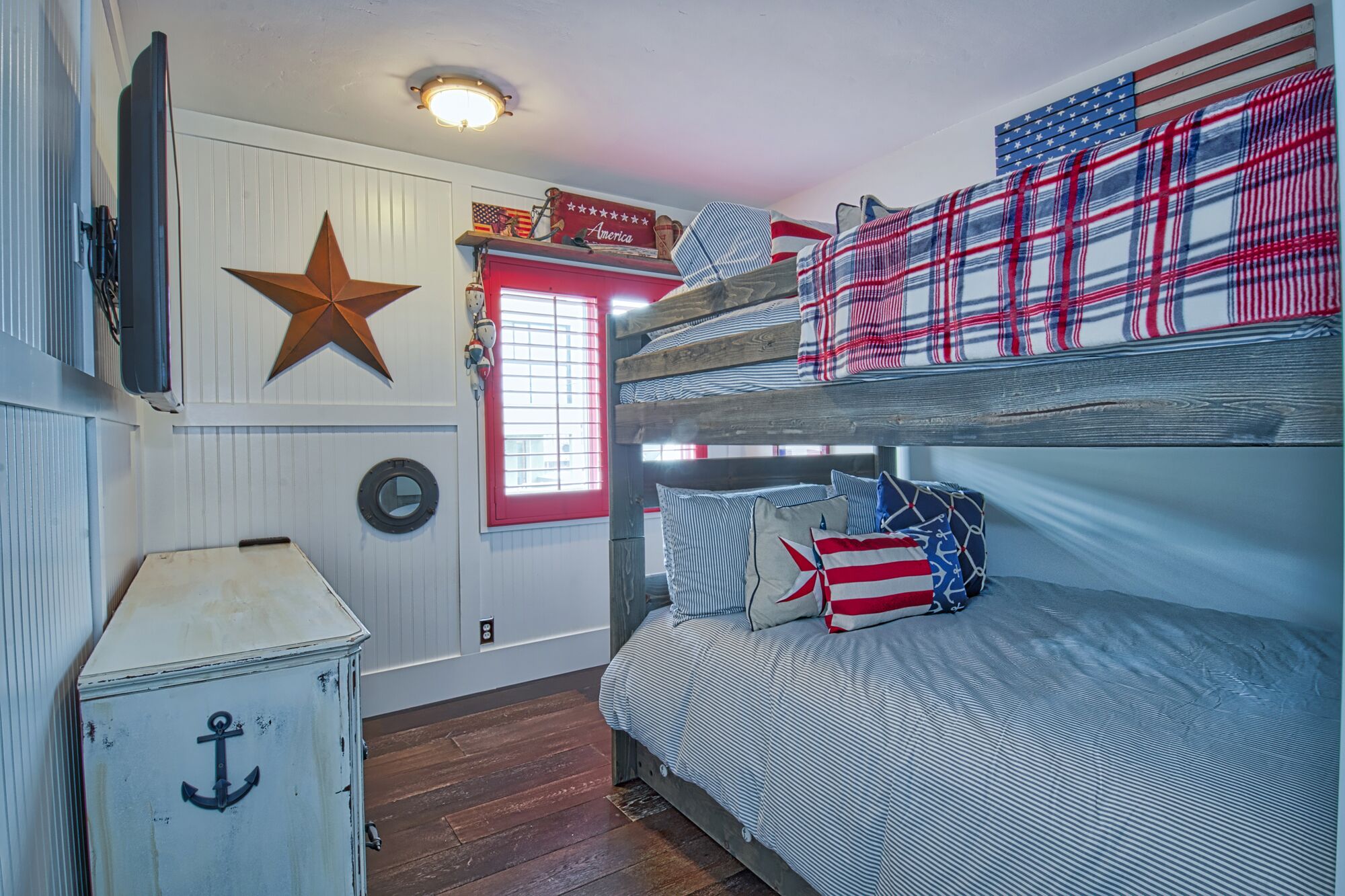 A bunk bed with striped bedding, a star decoration, a clock, and a small cabinet with an anchor design.
