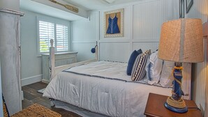 Een slaapkamer met een bed, een lamp, een ingelijste jurk en een houten lepel aan het plafond.