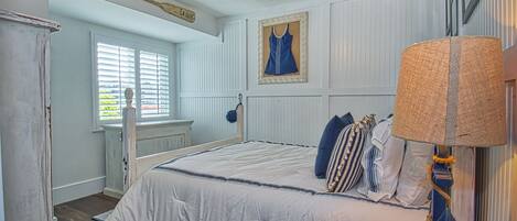 Un dormitorio con cama, lámpara, un vestido enmarcado y una cuchara de madera en el techo.