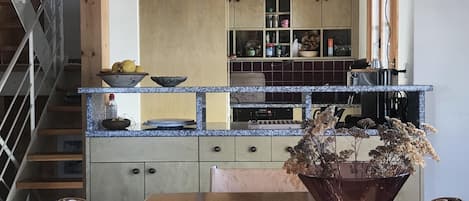 Una cocina con una mesa de madera, un florero con flores secas y una escalera.