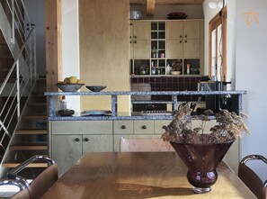 A kitchen with a wooden table, a vase with dried flowers, and a staircase.