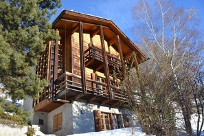 A multi-story wooden chalet with balconies, surrounded by trees and snow.