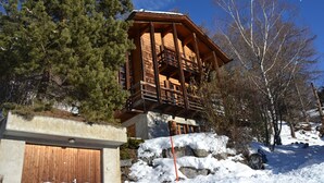 Una cabaña de madera con balcón, rodeada de nieve y árboles.